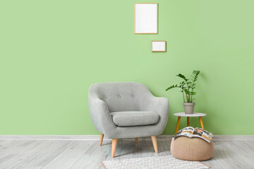 Grey armchair, pouf, table and blank frames hanging on green wall