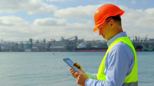 Port worker at sea ships construction. Customs officer checks information about freights on tablet against cisterns and cranes in docks side view