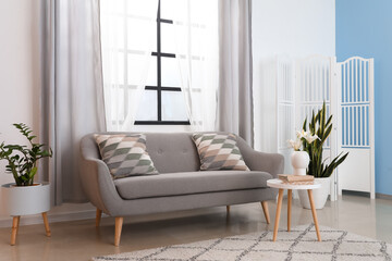 Interior of light living room with grey sofa and curtains