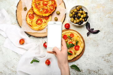 Woman taking photo of delicious mini pizzas on light background