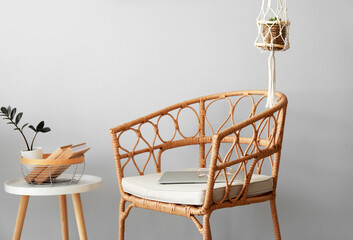 Wicker chair with laptop, eyeglasses and table near light wall