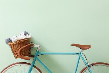 Stylish bicycle with wicker basket and flowers near green wall