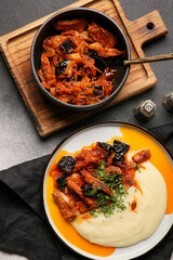 Plate with delicious mashed potatoes, gravy and beef stew with prunes in bowl on black background