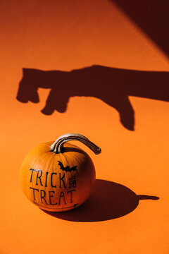 Hand shadow reaching for a orange decorated pumpkin 