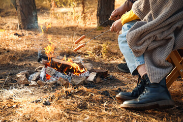 Friends roasting sausages on fire in autumn forest