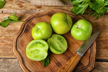 Board with fresh green tomatoes and knife on wooden background, closeup