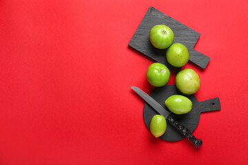 Boards with green tomatoes and knife on color background