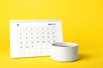 Flip paper calendar for May 2022 and cup of coffee on color background