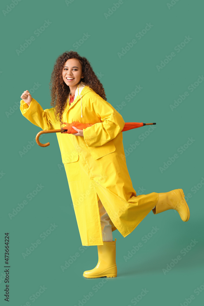 Canvas Prints young african-american woman wearing yellow raincoat and gumboots with umbrella on green background