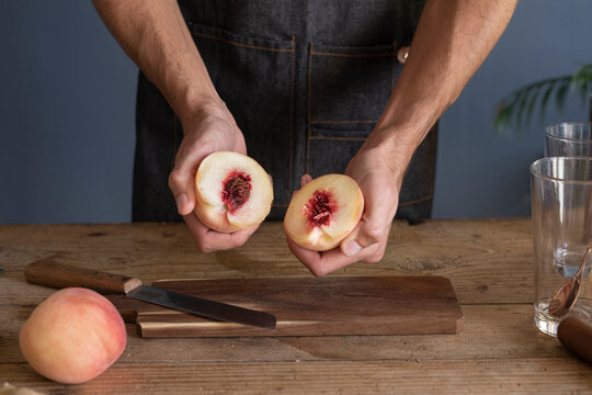 Man's Hands Cutting Fresh Peach On Wooden Board