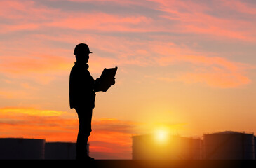 Silhouette of Engineer under inspection and checking oil storage tank, Engineer man in waistcoats and hardhats and with documents in oil storage plant