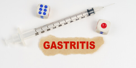 On a white surface lies a syringe, dice and a piece of paper with the inscription - GASTRITIS