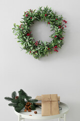 Table with gift boxes, fir tree branch and Christmas wreath with mistletoe hanging on light wall