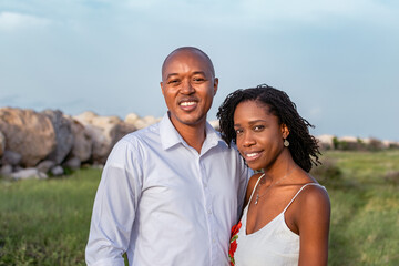 Young loving black couple standing close together outside, staring at camera smiling,  grassy meadow. Happy African couple outside, Jamaica, shot on the Palisadoes strip