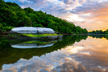 Rock in still water under a cloudy sunset