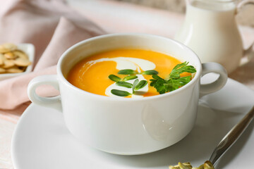 Pot with delicious pumpkin cream soup and seeds on table, closeup