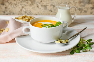 Pot with delicious pumpkin cream soup and seeds on white wooden table