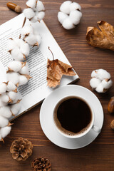Cup of coffee, opened book, cotton flowers and autumn decor on wooden background