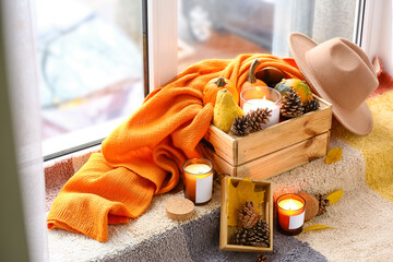 Burning candles in holders and autumn decor on windowsill in room