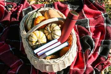 Picnic basket with books, pumpkins and thermos bottle on plaid in autumn park