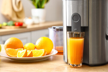 Modern juicer with fresh citrus fruits and glass of juice on table in kitchen