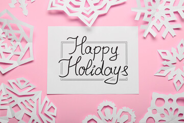 Paper snowflakes and greeting card with text HAPPY HOLIDAYS on color background