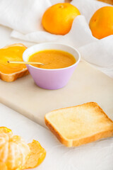 Bowl of tasty tangerine jam and bread on table, closeup