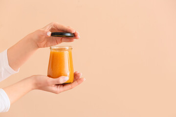 Female hands with jar of tasty tangerine jam on color background