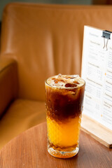 A glass of layered bumble coffee with caramel and orange juice, small wooden table and yellow armchair