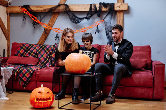 Parents with son smiling and drawing face on pumpkin 