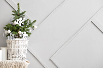 Beautiful Christmas tree in basket decorated with snowflakes and balls on table near light wall