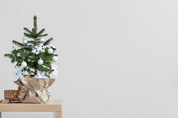 Beautiful Christmas tree decorated with snowflakes and balls on table near light wall