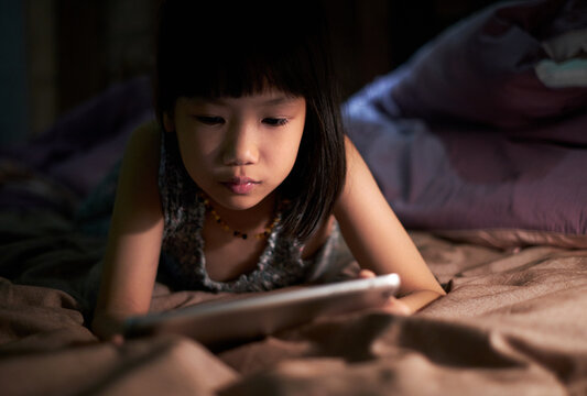 Asian little girl looking at tablet computer on the bed