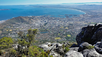 From the top of Table Mountain, you can enjoy views of Cape Town, the Atlantic Ocean, Signal Hill. In the foreground there are huge gray boulders, bushes. South Africa