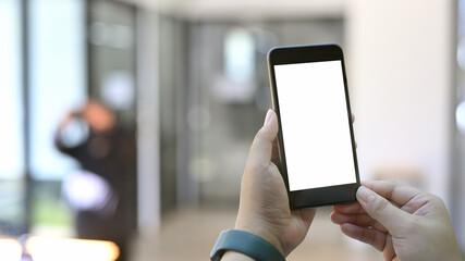Close up young man holding smart  with blurred coffee shop background.