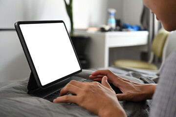 Young man in pajamas browsing internet with computer tablet on his bed.