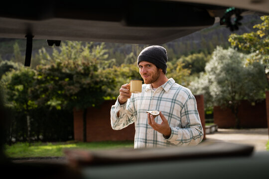 Young man having coffe and toast in van on the road
