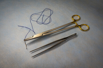 a surgical suture is clamped in a needle holder and a pair of tweezers lies next to it