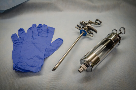 an instrument for performing a prostate resection lies next to blue medical gloves and a glass bulb syringe