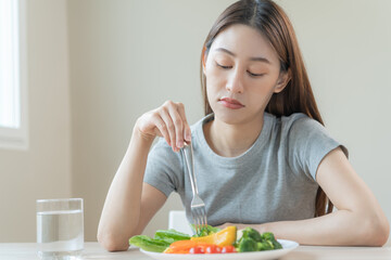 Obraz na płótnie Canvas Diet in bored face, unhappy beautiful asian young woman, girl on dieting, holding fork in salad plate, dislike or tired with eat fresh vegetables. Nutrition of clean, healthy food good taste.