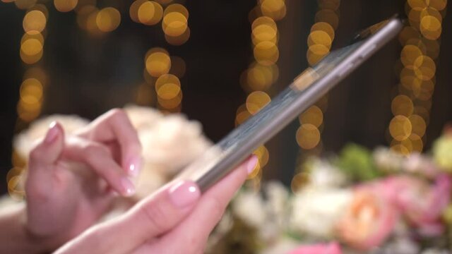 Business lady touches portable ipad computer device screen on cozy flower bed background. Zoom focus on female hands and fingernails. Closeup filming of sliding and swiping fingers on surface tablet.