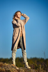Beautiful young attractive girl in coat against the blue sky. Enjoy Nature and autumn sun warmth