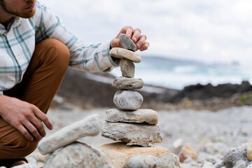 Fototapeta premium Man doing Zen balanced stones stack on beach