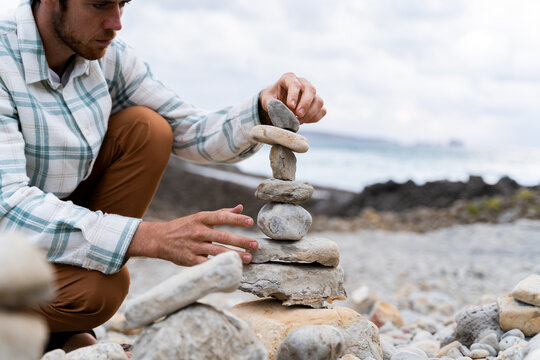 Man doing Zen balanced stones stack on beach