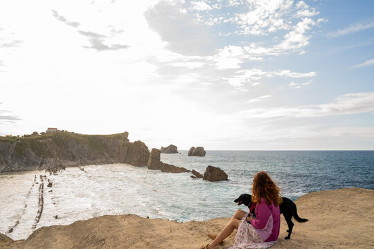 Woman with dog  looking at phone on cliff by the sea