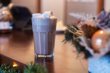 Cocoa with marshmallows in a transparent glass in a coffee shop on the background of New Year's decoration.