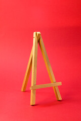 Easel for artists miniature on bright red background. Art minimal concept.