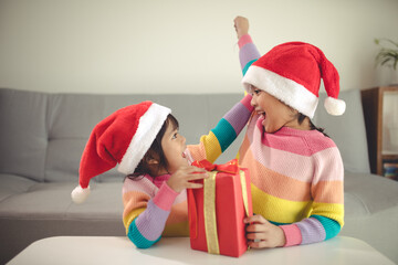 Merry Christmas happy sibling girls with a gift at home