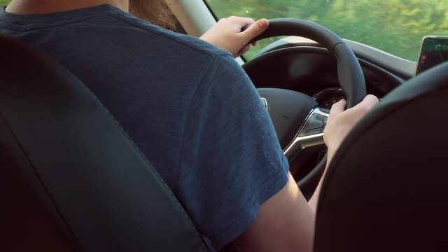 The driver behind the wheel of the car, controls the car, holds the steering wheel with both hands. Long drive. View from the rear from the passenger seat to the driver who drives the car.