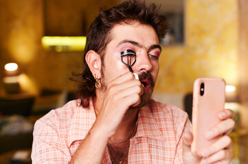 Young man curling his eyelashes at home